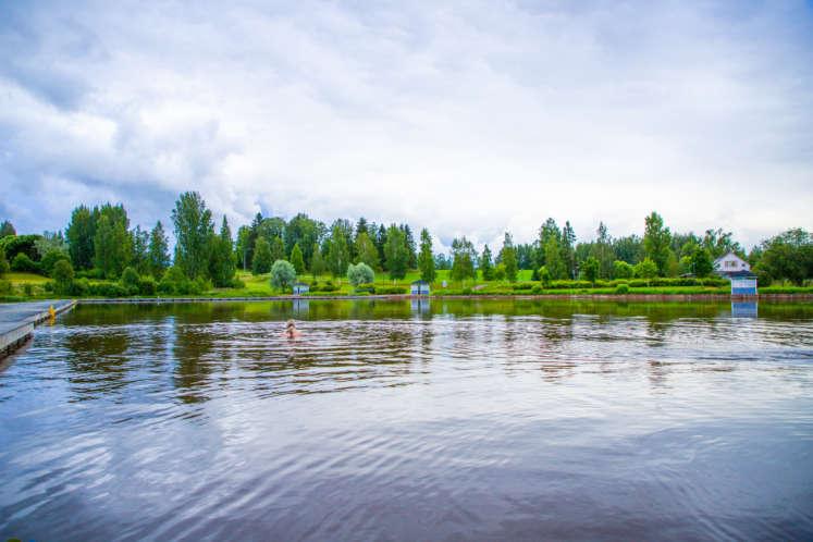 Meijerin uimaranta. Etualalla lampi, jossa ihminen ui. Taka-alalla puita ja puistoaluetta. Sää on pilvinen.