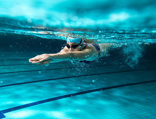 Uimari sukeltaa uima-altaassa. Kuva veden alta.